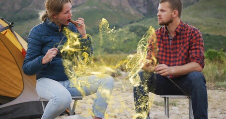 Roasting snack skewers camping couple sitting on folding stools at mountain campsite, yellow tent