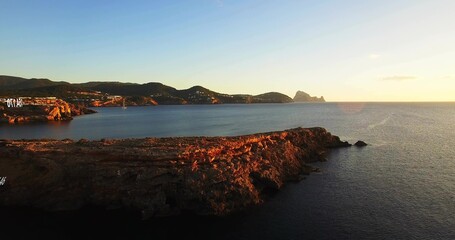 Basking rocky headland glowing at seaside, featuring hillside sign, hillside buildings and calm sea
