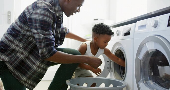 Helping parent and child loading laundry into front-loading washer in laundry room with gray basket