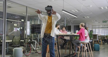 Gesturing man wearing VR headset interacting with virtual graphics in office space with bicycle