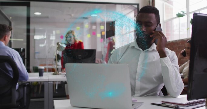 Talking adult man calling on smartphone while typing on laptop at open-plan office, copy space - Powered by Adobe