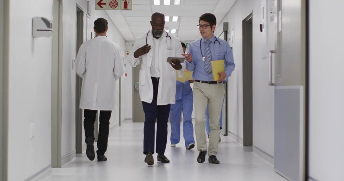 Walking male doctors checking tablet in hospital corridor, with lab coats and stethoscopes