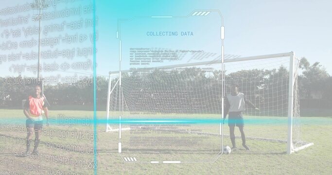 Standing duo wearing vests monitoring AR interface on grass soccer field, with goal and ball - Powered by Adobe