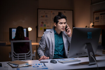 Businessman working computer while talking on phone late