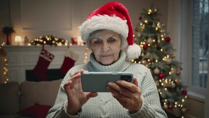 senior woman holding a smartphone while Christmas decorations are visible in the background. Concept of digital connection and staying in touch during the holiday season. Online video call 