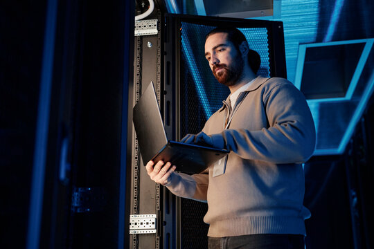 Engineer using laptop near supercomputer in server room