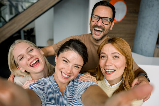 Team taking selfie with mobile phone smiling in modern office