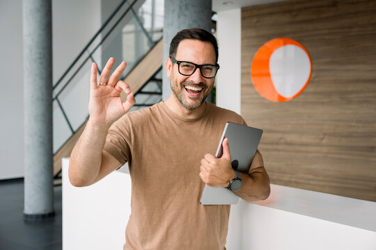 Confident business consultant smiling with tablet making ok gesture indoors