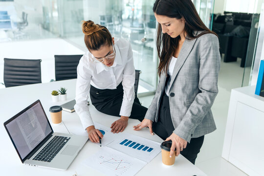 Businesswomen discussing strategy with laptop and charts at office