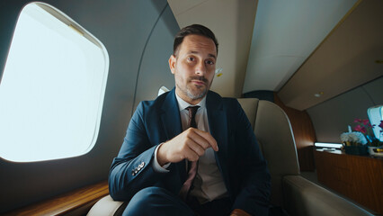 Confident businessman in a dark suit seated in a private jet cabin, posing for a portrait that conveys luxury, executive travel, success and high-end corporate status