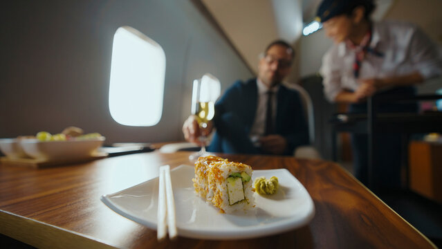 Man in a business suit receiving a sushi meal and a glass of champagne from a flight attendant while traveling in the luxurious cabin of a private jet, emphasizing comfort and high-class service