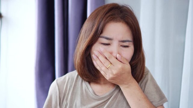 Unwell Asian woman suffering from nausea in bed, feeling sick and wanting to vomit. Concept of food poisoning, morning sickness, pregnancy symptoms, and health discomfort