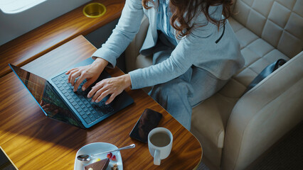 Businesswoman typing on a laptop computer while flying in a luxurious private jet, combining work and travel in a high-class, executive environment with a cup of coffee and dessert on the table