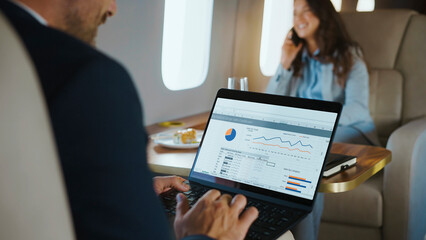 Business executive working on laptop displaying sales dashboard charts while traveling by private...