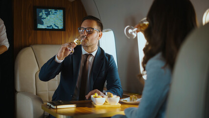 Businessman and woman passengers are traveling in luxury, drinking champagne and celebrating success during a private jet flight, enjoying premium service and comfortable travel