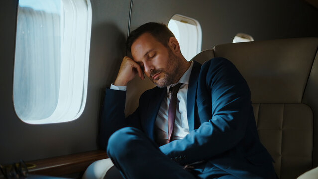 Businessman resting in his suit and tie while traveling on board a luxury private jet, experiencing exhaustion from a challenging business trip and sleeping soundly in the comfortable cabin