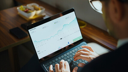 Businessman working on a laptop, monitoring currency pairs and analyzing financial charts on the screen, engaging in online trading and investment activities