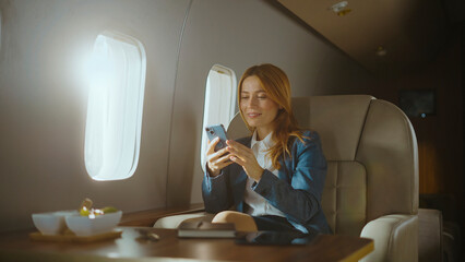 Engaged businesswoman sitting inside a private jet using her smartphone, connecting during business travel, representing luxury, success, and global communication