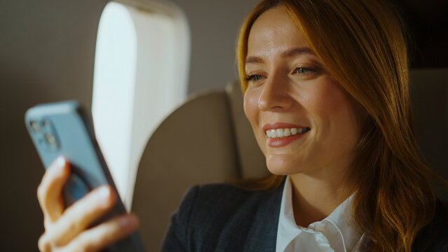 Businesswoman on a plane smiling as she uses her smartphone to work or stay connected, enjoying business travel while checking messages, social media, or making calls - Powered by Adobe