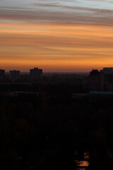 Cityscape at sunset with vibrant orange and pink sky and soft clouds above silhouetted buildings. Urban skyline and evening nature concept.