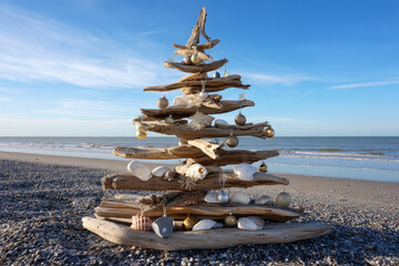 Handmade Christmas tree made of driftwood, adorned with seashells and coastal ornaments on a beach setting. A chic, creative, and beautiful Christmas or New Year tree for the interior 