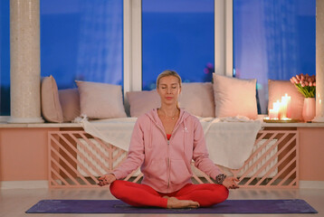 A yoga coach in red sportswear explains breathing techniques to students, demonstrating mindfulness and calm concentration during an evening session in a bright urban studio.
