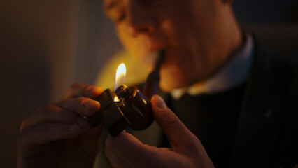 Gentleman's hands holding a classic metal lighter, creating a bright flame to ignite a tobacco...
