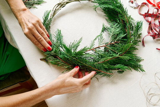 Hands of mature woman making Christmas wreath on table