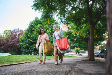 Obraz premium Friends walking through park carrying shopping bags on a sunny day