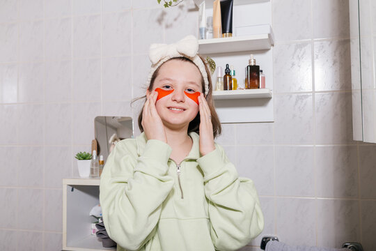 Smiling teen with eye patches and bow headband does skincare in bathroom