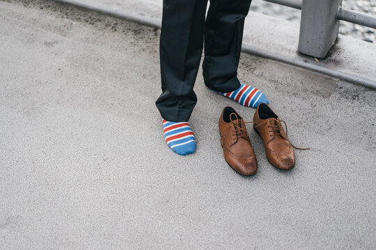 Young man in socks standing on street with leather shoes in front of him