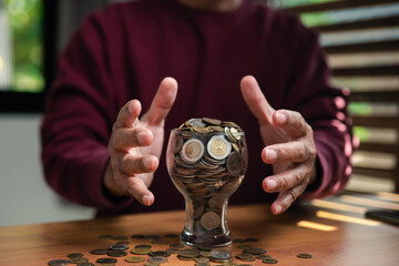 Close-up of hands protecting a glass filled with coins on wooden table, symbolizing financial security, savings, investment, and wealth protection concept for personal finance and money management.