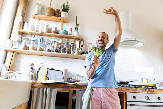 Joyful man enjoying dancing and singing while cooking at home