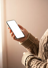 Woman in a cozy sweater holding a smartphone with a blank screen mockup