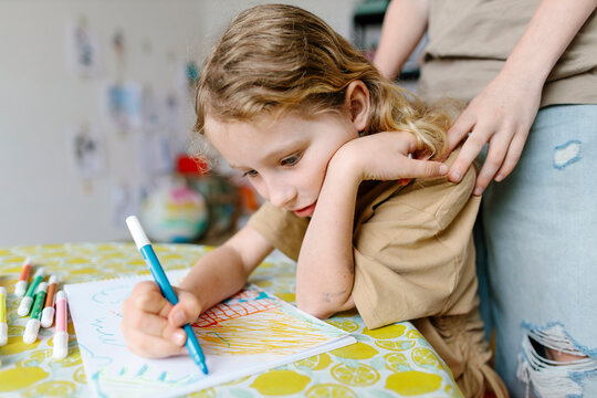 Child focused on drawing with supportive presence nearby