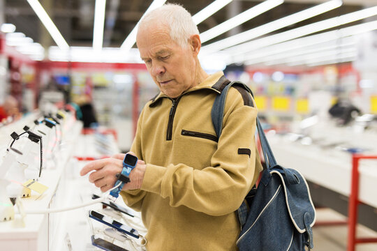 elderly man examines smart watch in showroom of electronics store