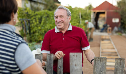 Two gardeners friendly talking outdoors next to wooden fence of country estate on day