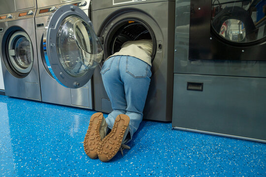 Young woman kneeling inside of washing machine at laundromat