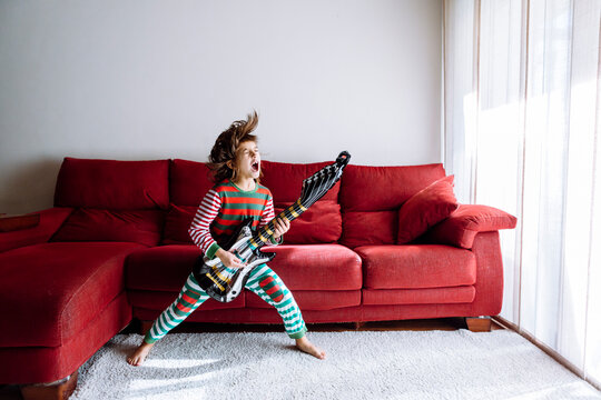Happy girl playing guitar against sofa in living room