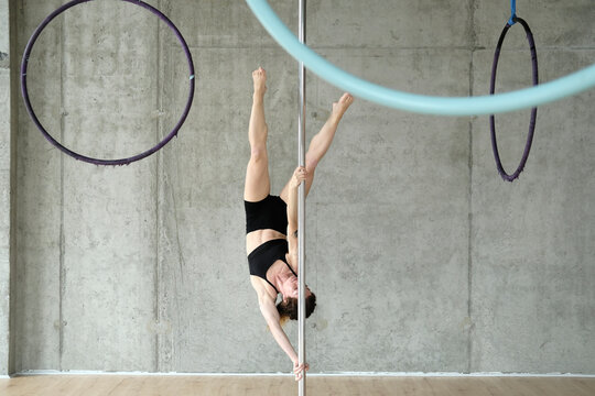 Woman practicing gymnastics on pole in front of concrete wall