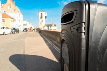 Shallow focus of a typical, new designed litter bin seen on a sunny promenade on the coast of Suffolk, UK. Next to the wall on the right is the pebble beach.