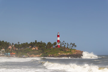 Striking Red and White Striped Lighthouse on a Tropical Cliff Overlooking the Rough Waves