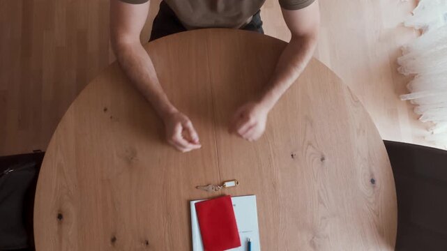 A man sits at a wooden table with documents, a red folder, and keys, symbolizing the final step of a property handover or signing. Ideal for real estate, leasing, and ownership agreement themes.