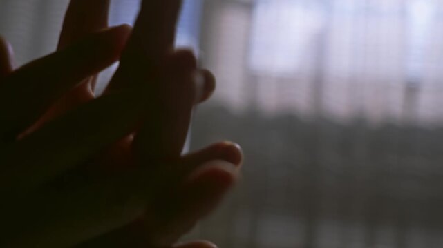 Fingers clasp in emotional gesture in moody room shadows close-up