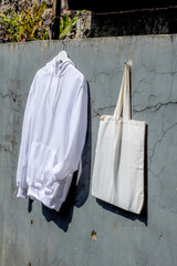 Clean White Hoodie and Tote Bag Hanging Against Rustic Wall