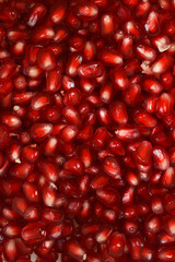 A close-up of numerous red, glossy pomegranate arils tightly packed together, filling the entire frame to create a vibrant food texture