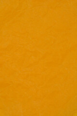 A vertical close-up of a warm, orange-yellow surface featuring a prominent, dense texture of soft creases and random folds, resembling crushed paper