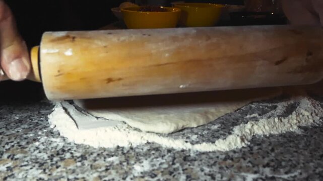Chef or home cook using a rolling pin to make soft white and brown colored fluffy pizza douch on home kitchen countertop or table in slow motion with white colored fluffy flour around. Shallow depth.