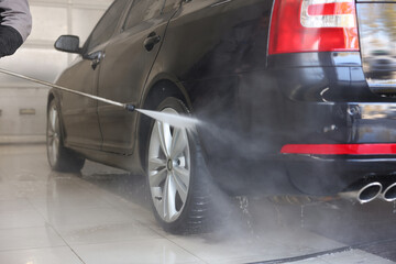 Man washing auto with high pressure water jet at car wash, closeup