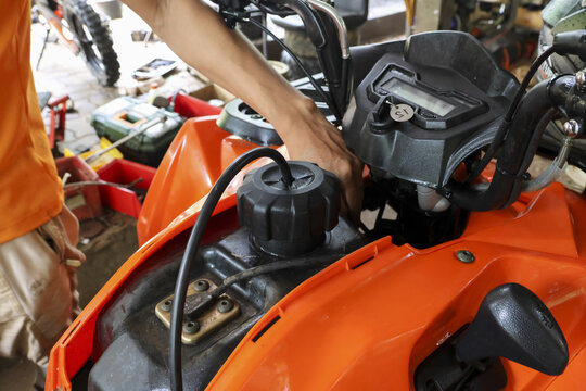 Focused man doing atv repair and maintenance on an orange vehicle engine in garage. skilled mechanic at work, this powerful quad bike requires professional service